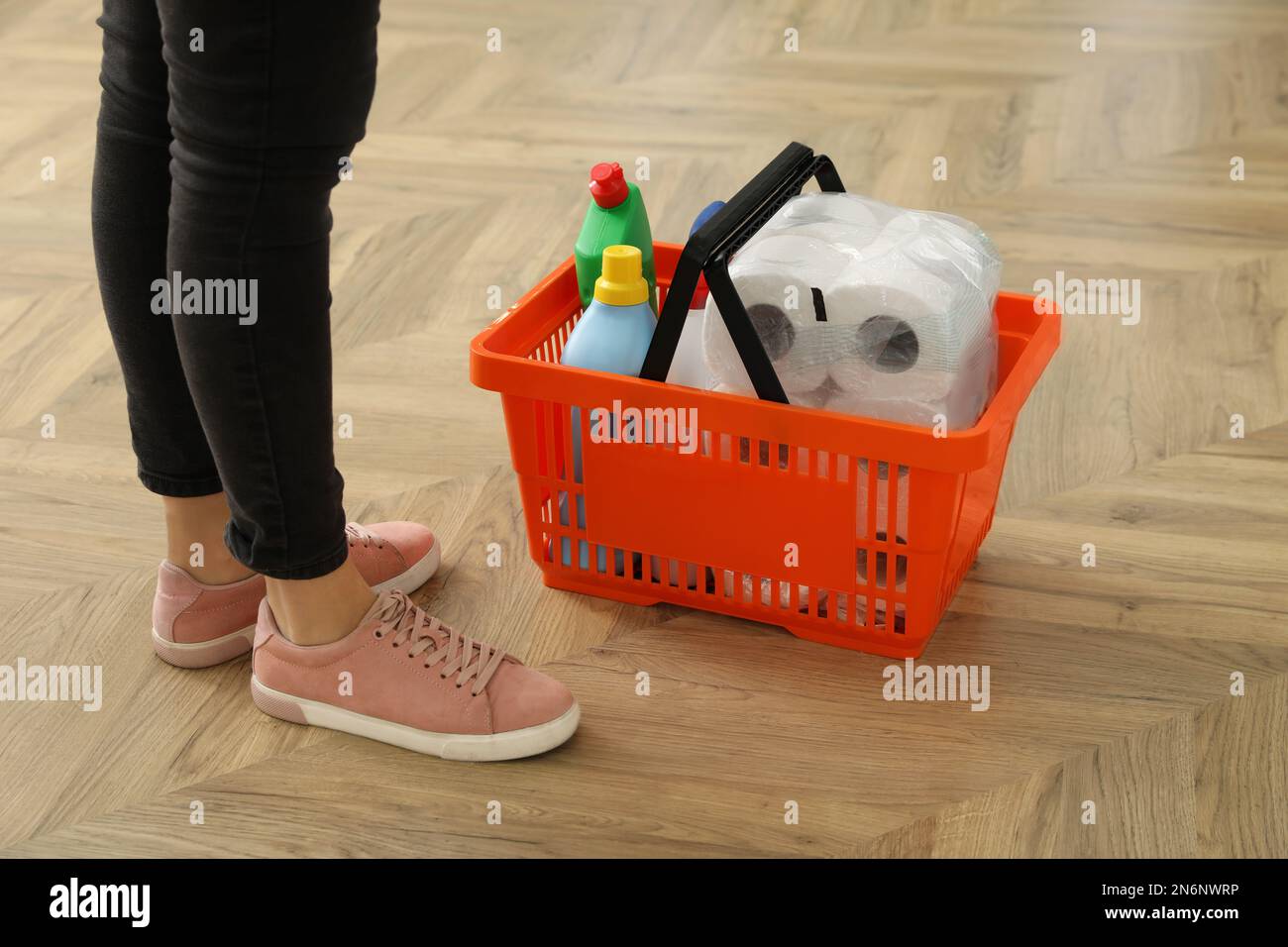Woman and shopping basket with household goods on wooden floor, closeup Stock Photo