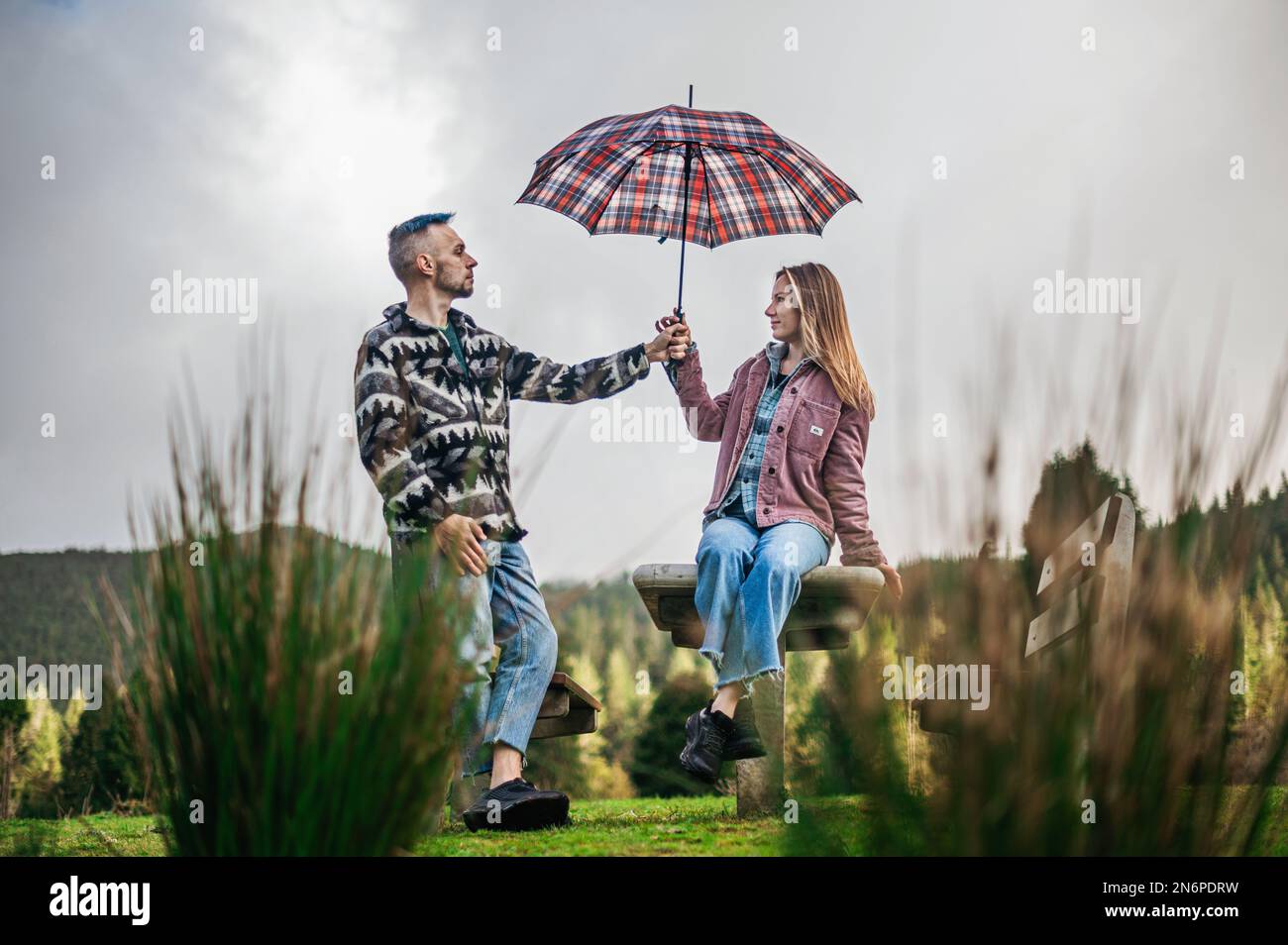 Loving couple sits on a bench with the man holding a patterned umbrella above the woman Stock Photo