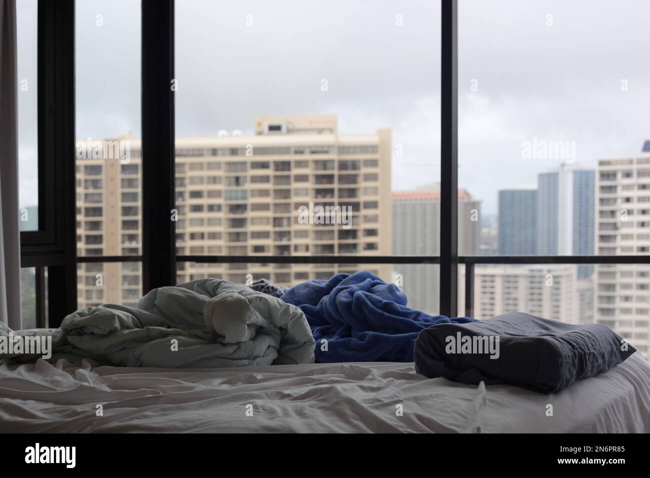 Unmade bed with messy blankets and pillow in hi-rise apartment with city view Stock Photo