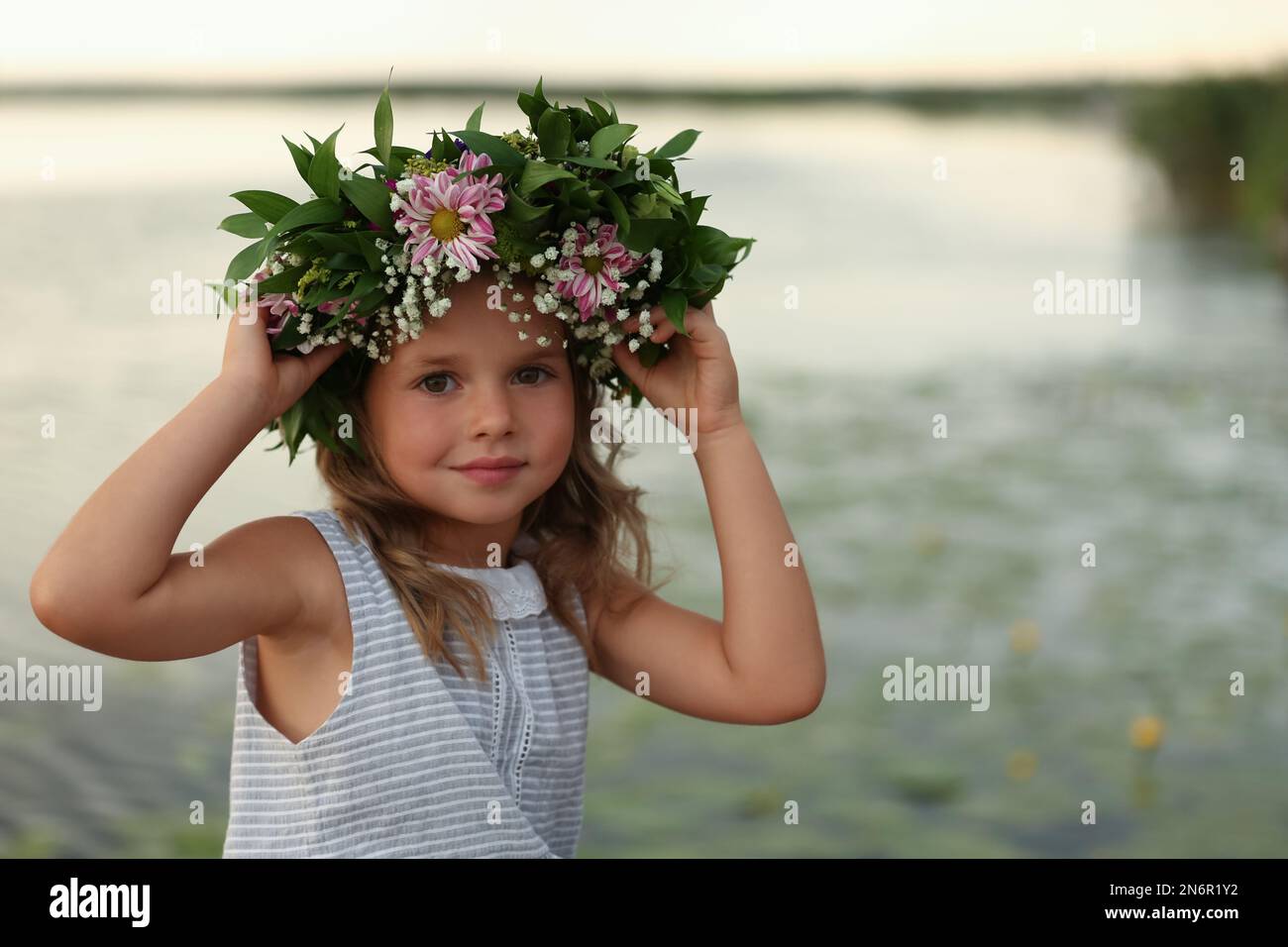 Cute little girl wearing wreath made of beautiful flowers near river ...