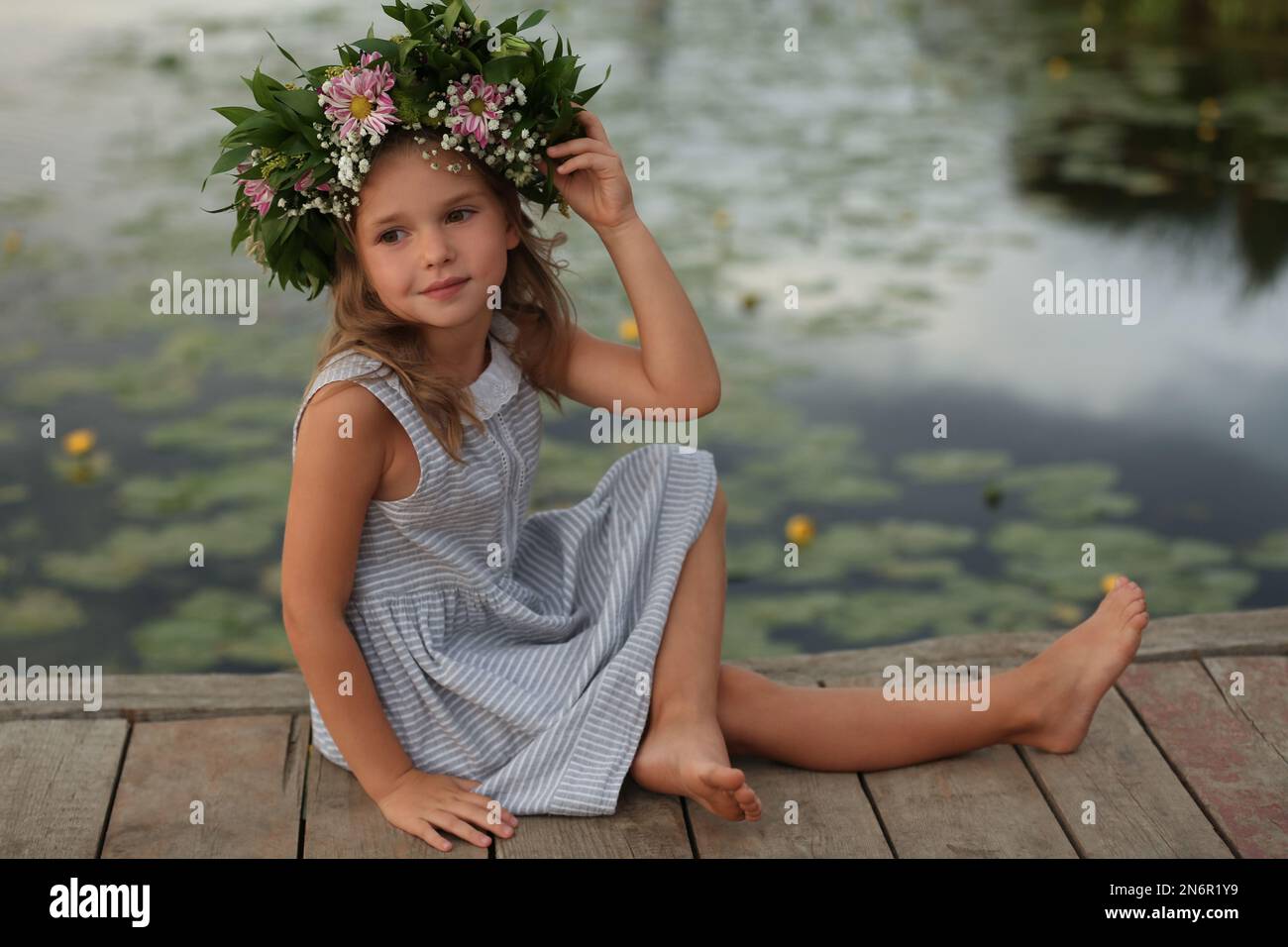 Cute little girl wearing wreath made of beautiful flowers on pier near ...