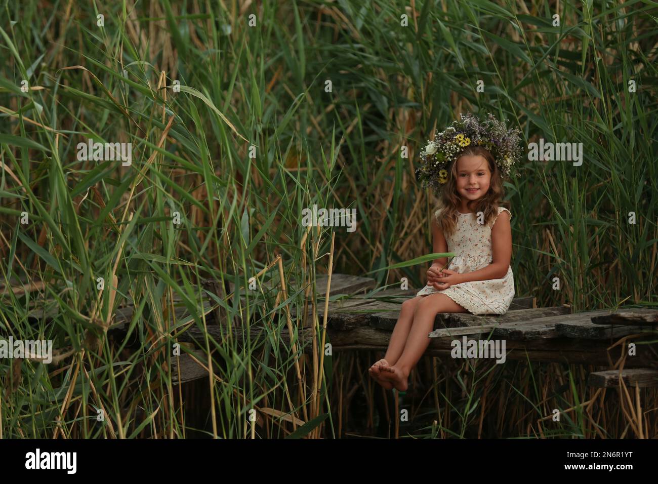 Cute little girl wearing wreath made of beautiful flowers on wooden ...