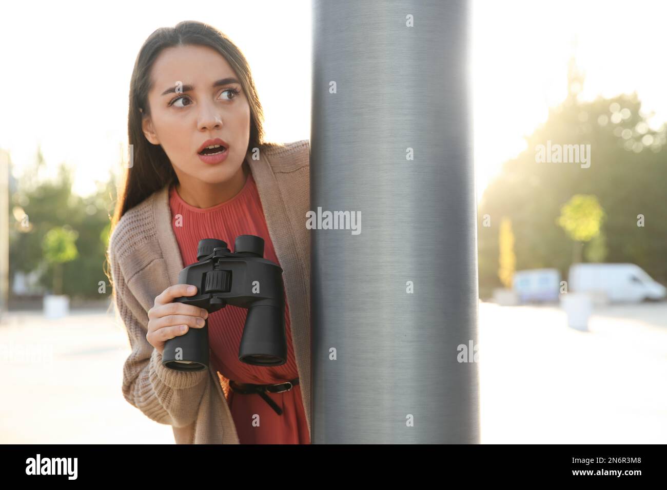 Jealous woman with binoculars spying on ex boyfriend outdoors Stock Photo