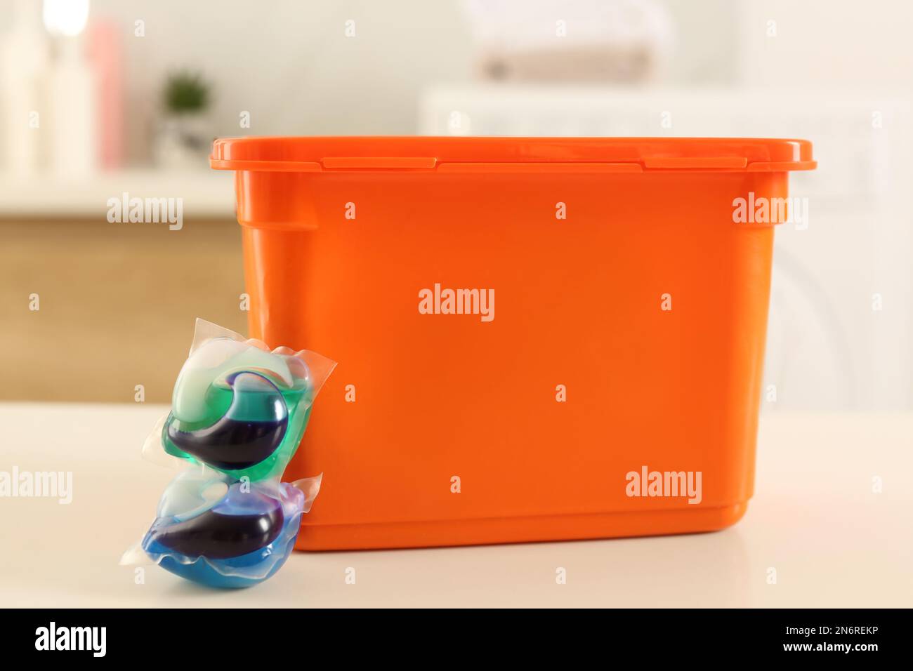 Laundry container and washing detergent capsules on table indoors Stock Photo