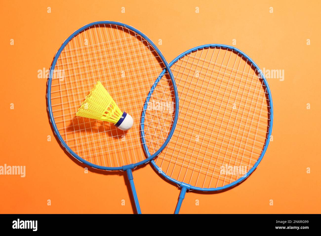 Badminton rackets and shuttlecock on orange background, flat lay. Space ...