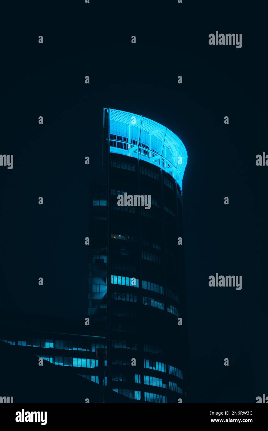 A vertical shot of illuminated blue modern office building at night with glass windows Stock Photo