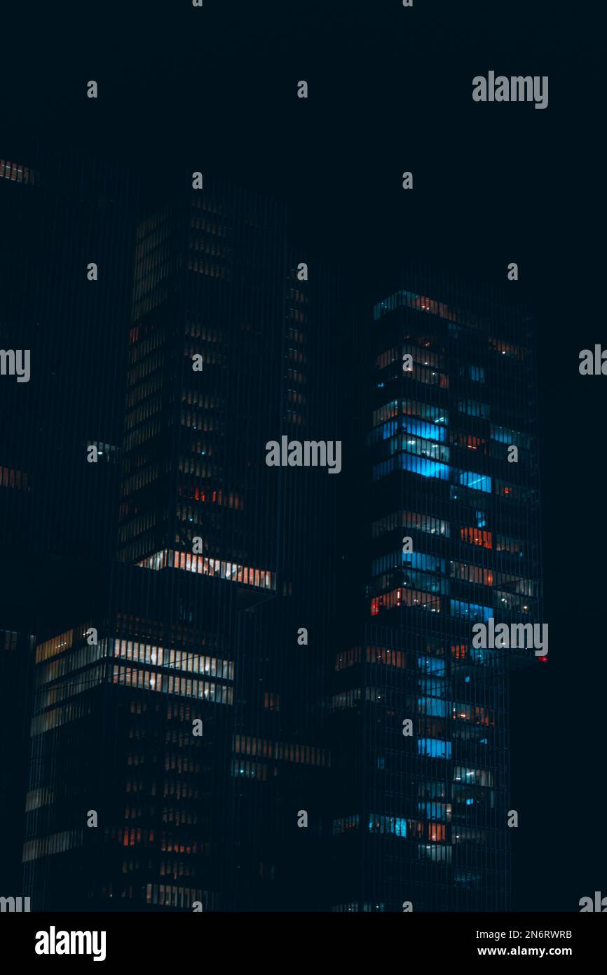A vertical shot of illuminated modern office buildings at night with glass windows Stock Photo