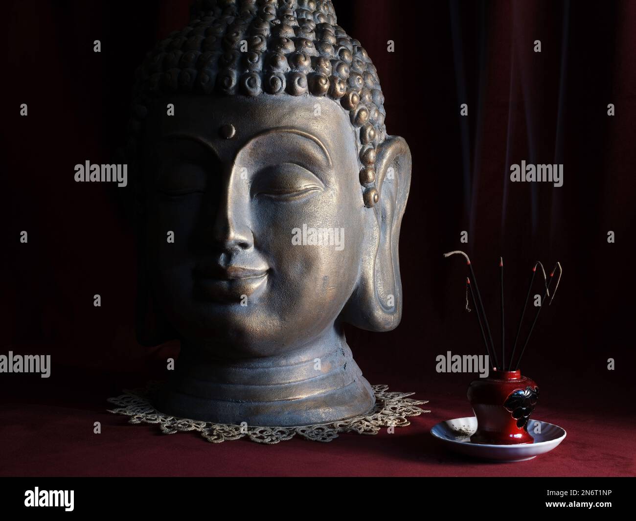 Buddha head in natural light with burning incenses, photo taken indoors Stock Photo
