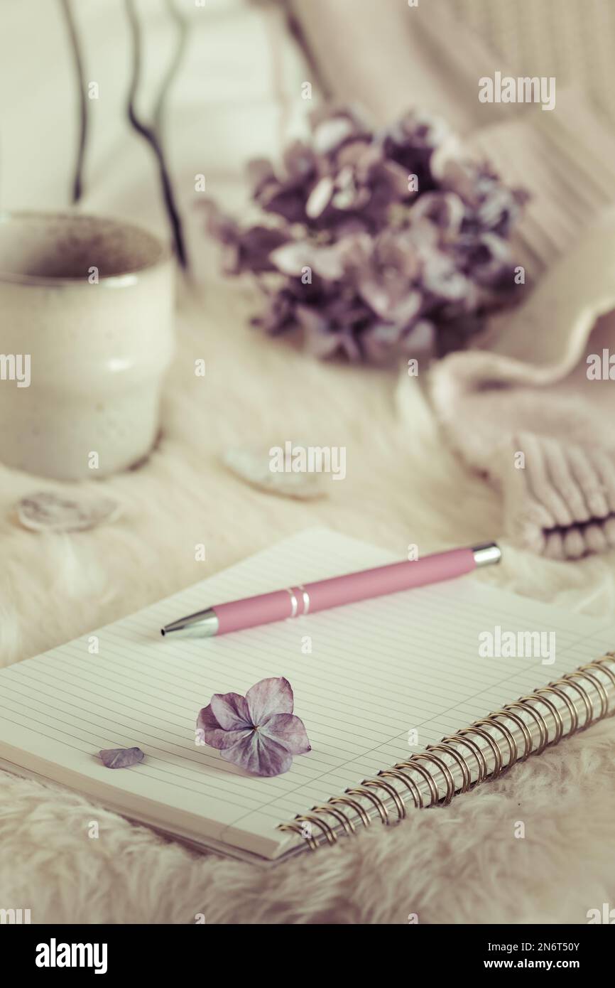 Cozy coffee break scene with notebook and pen, cup and wool fabric, cream and lilac colors, vintage style, vertical Stock Photo