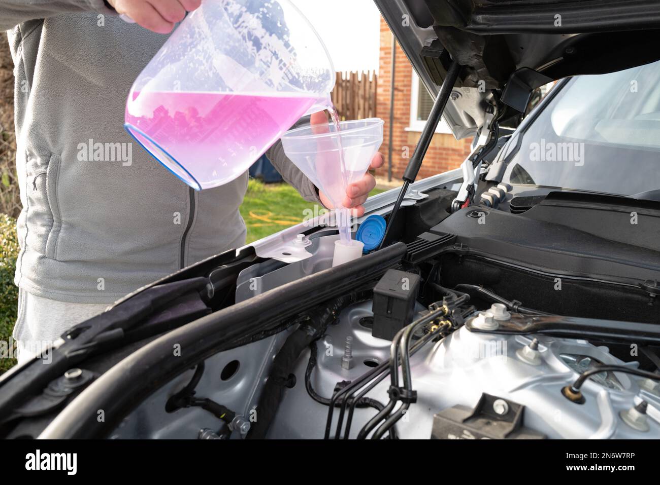 Shallow focus of windscreen washer fluid being poured by its owner into