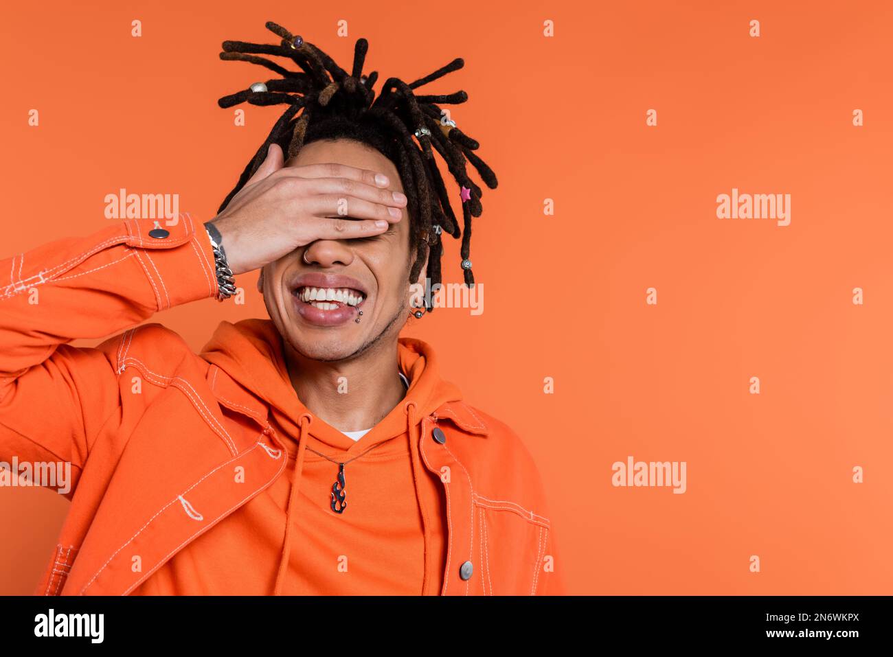 happy multiracial man with dreadlocks and tattoo covering eyes isolated on  coral background Stock Photo - Alamy