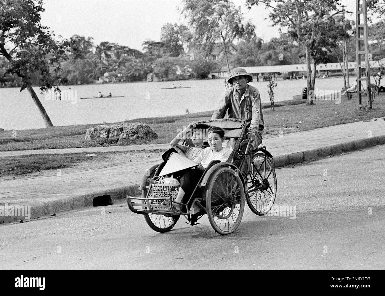 A Vietnamese cycle taxi carries a par of Vietnamese women around a lake ...