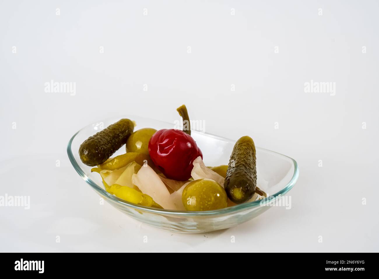 Mixed gherkins, sauerkraut, pepper, tomato and cucumber pickles on glass plate isolated on white background. Stock Photo