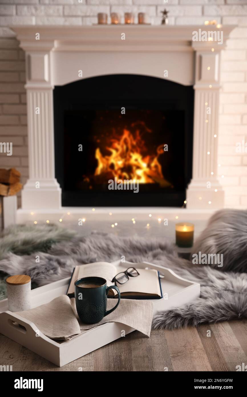 Cup of hot drink and book on blanket near fireplace indoors