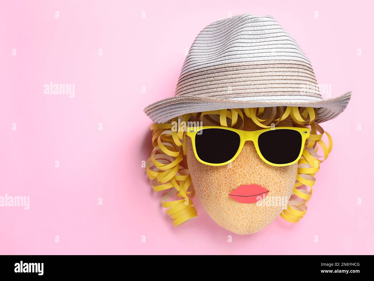 Funny face made of melon, hat and sunglasses on pink background, top