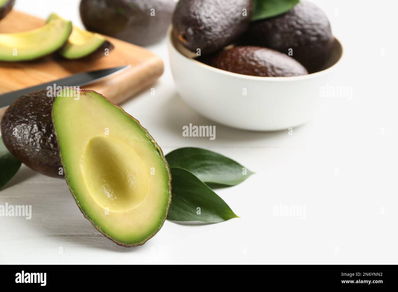 Whole and cut avocados with green leaves on white table Stock Photo - Alamy