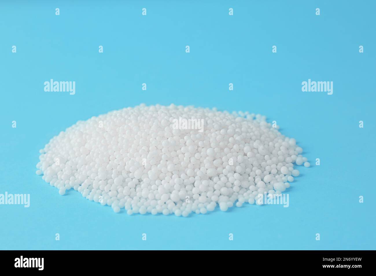 Pellets of ammonium nitrate on light blue background, space for text