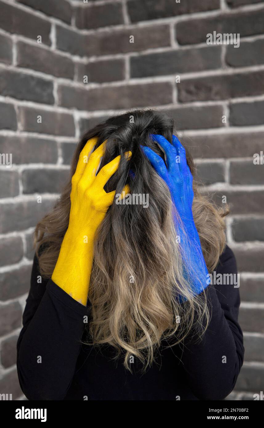 unrecognizable woman with hair covering her face in desperation holds head in hands, painted in colors of Ukrainian flag. suffering of civilians. Stop Stock Photo