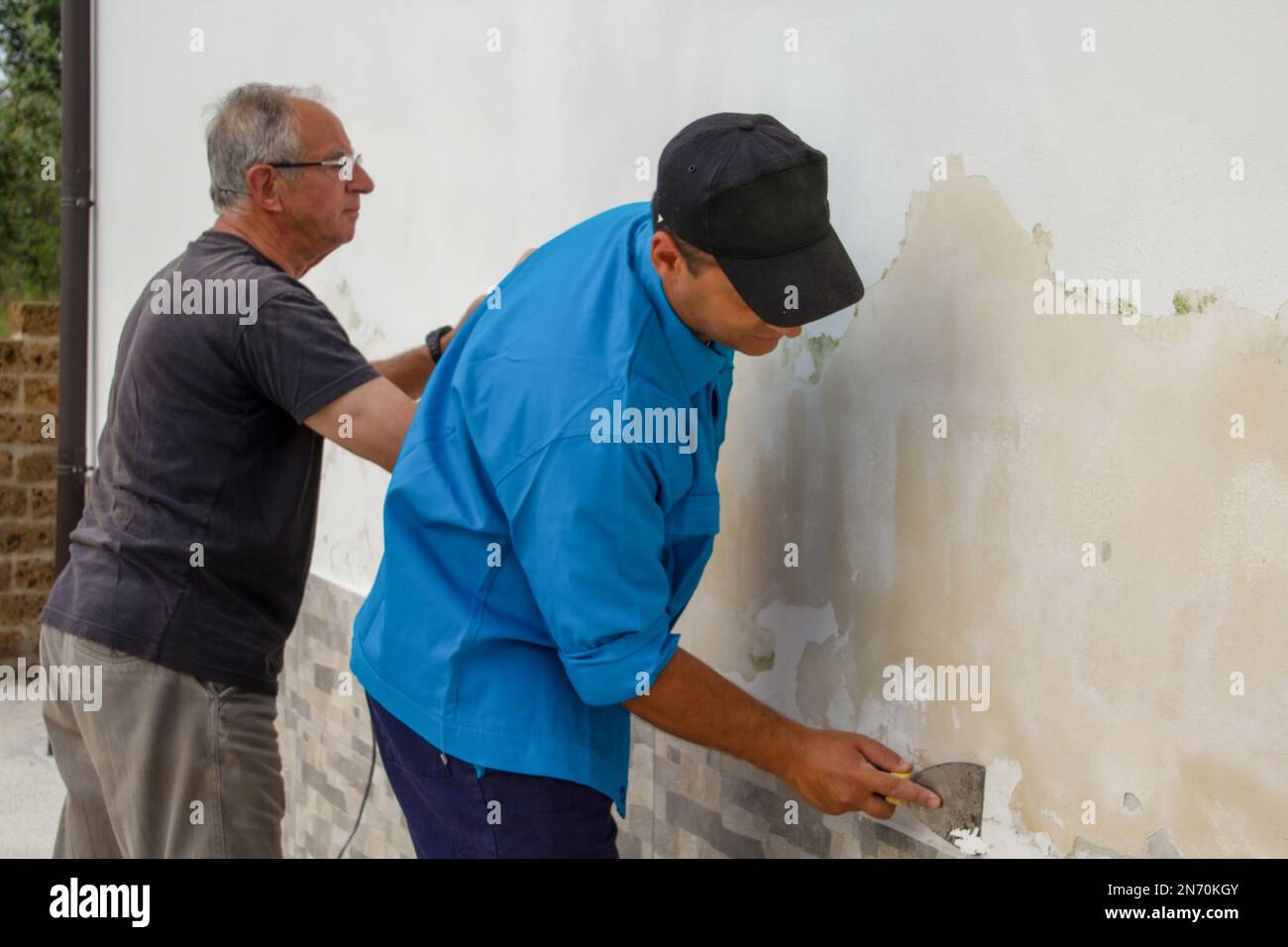 Image of two male construction workers sanding and cleaning a wall of mold. Rising damp problem. Stock Photo