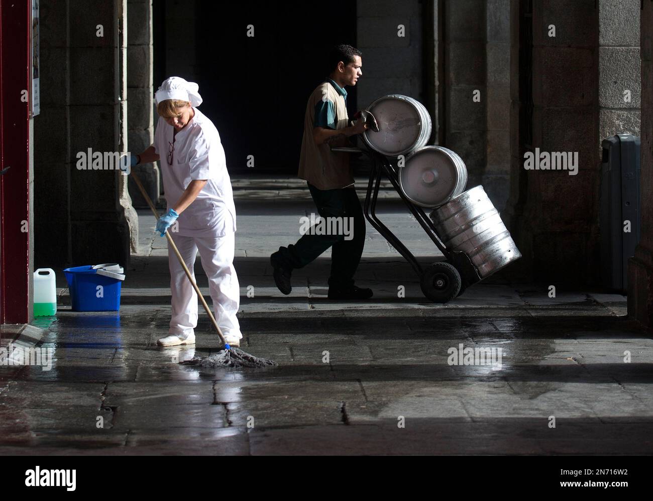 A worker delivers beer barrels as another mops the floor outside a bar