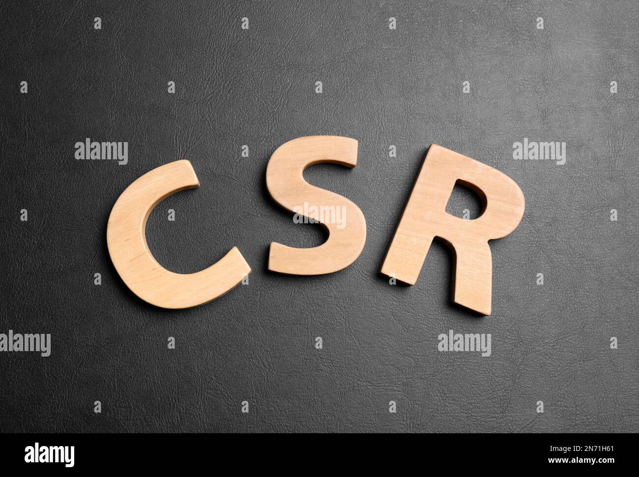 Wooden letters CSR on black background, flat lay. Corporate social ...