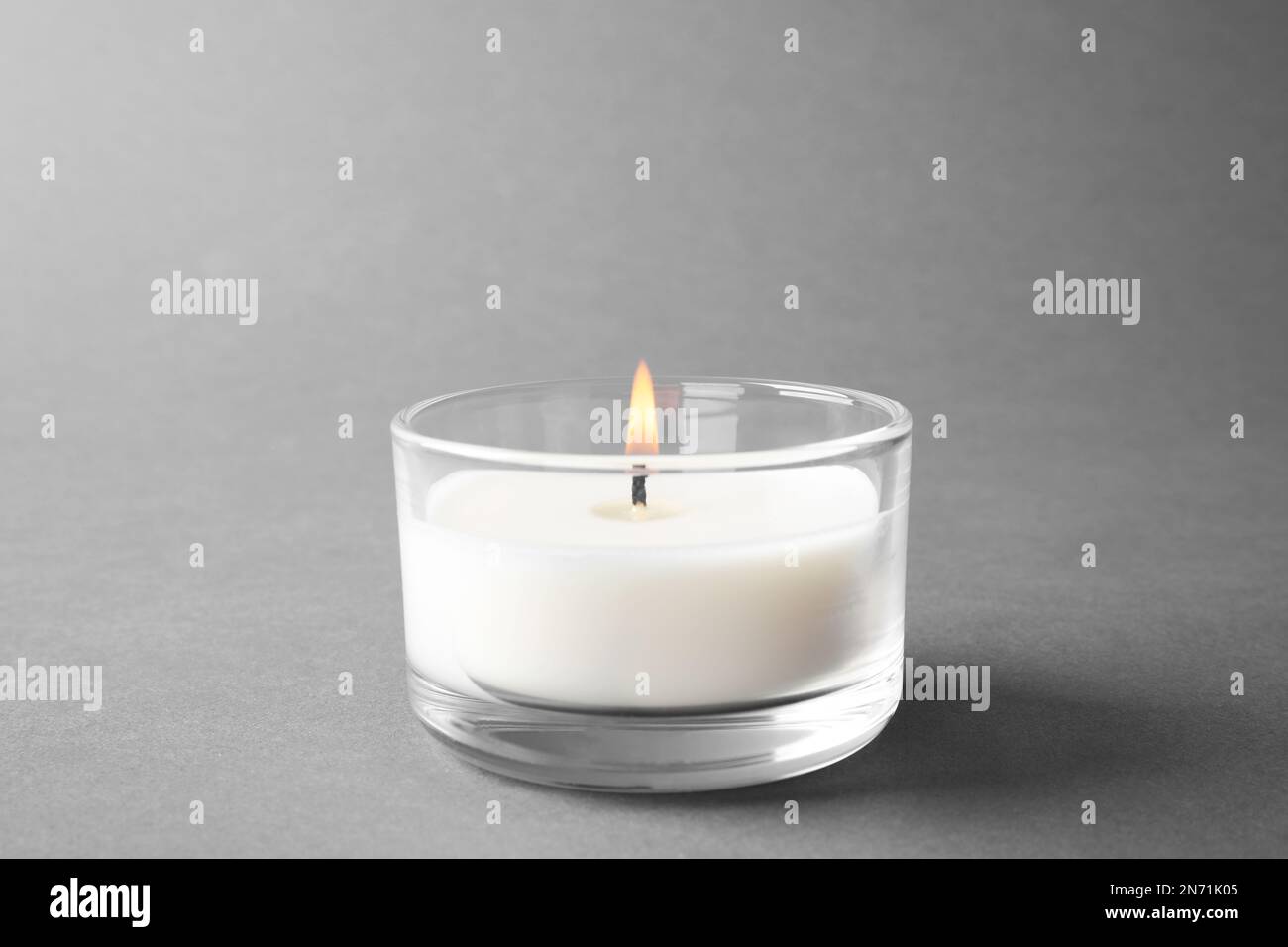 Burning small wax candle in glass holder on grey background Stock Photo