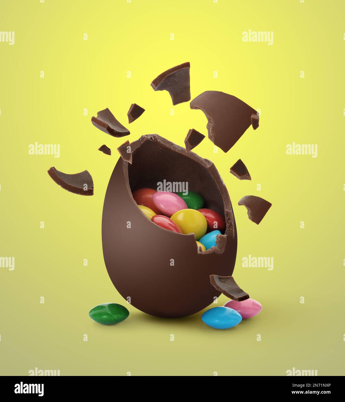 Broken chocolate egg with candies on yellow background Stock Photo