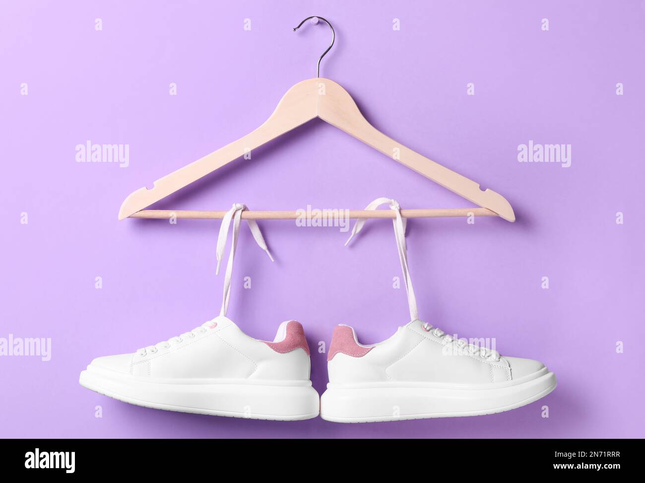 Stylish sneakers with white shoe laces hanging on wooden hanger against violet background Stock Photo