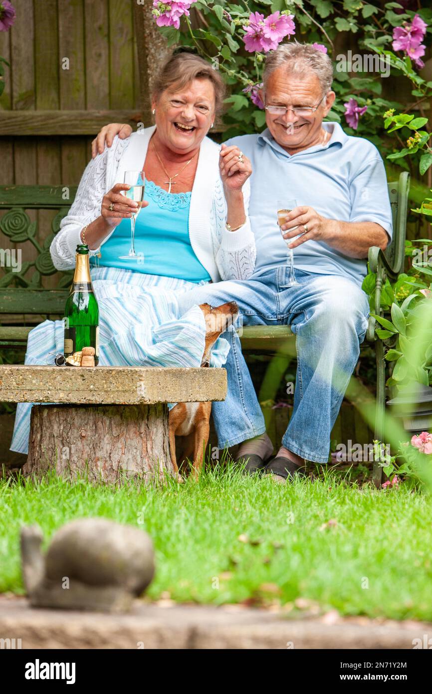 Retirement: Cheeky Dog. A candid moment of delight from a senior couple being surprised by their pet in the garden. From a series of related images. Stock Photo