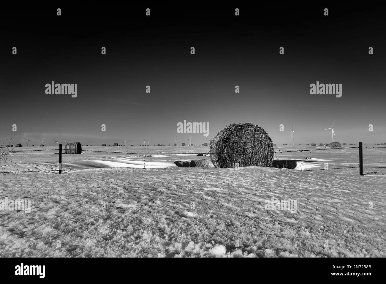 Hay bales and wind turbines line the snow covered horizon near Limon