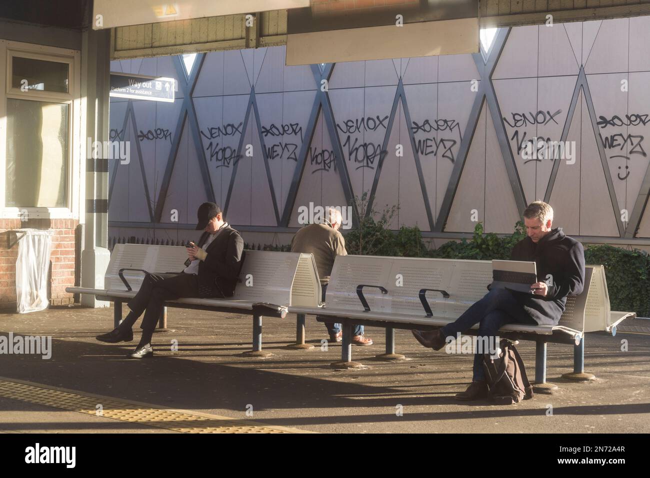 Three people looking at their devices while waiting for a train