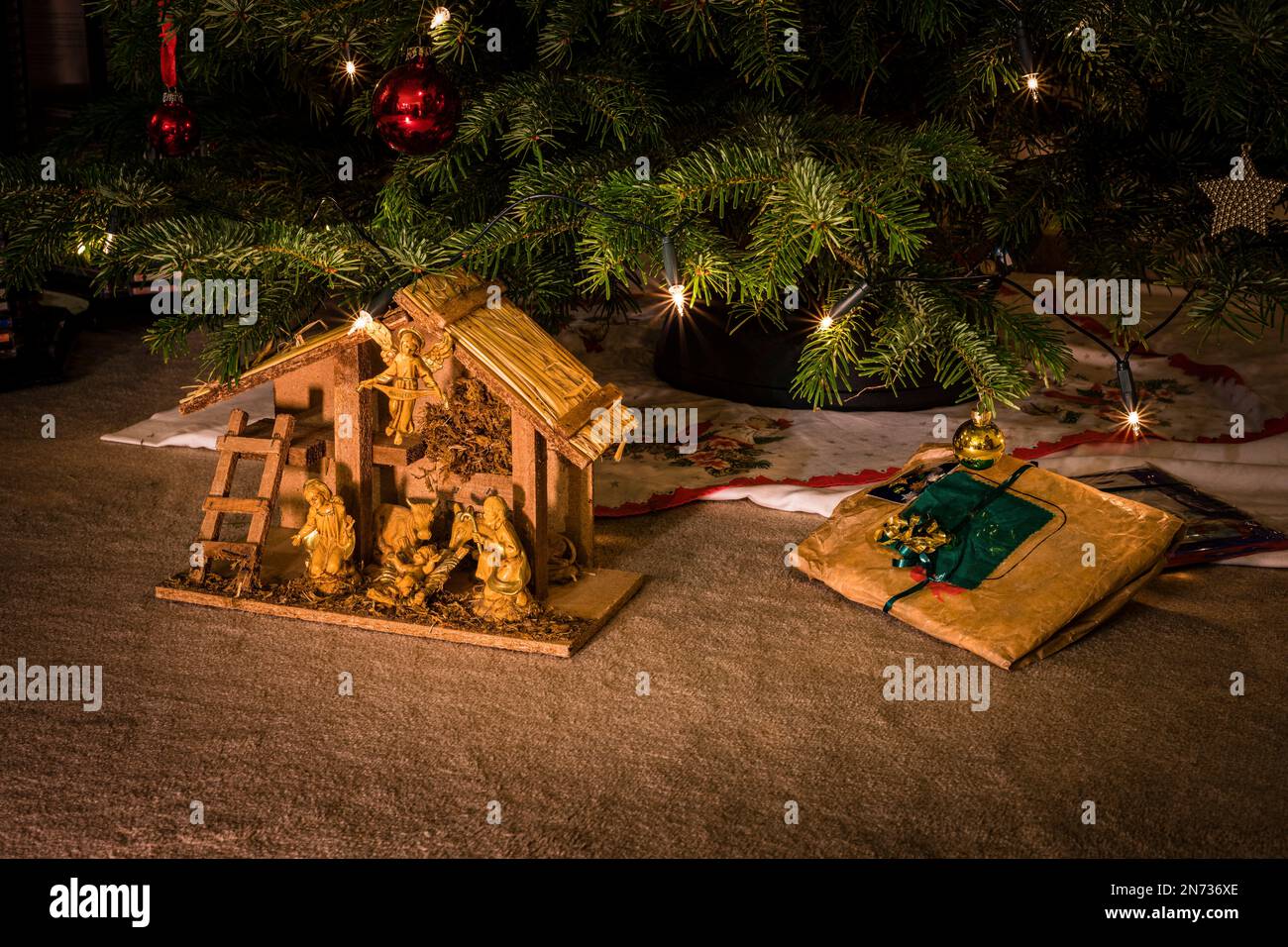 Nativity scene with holy family and animals under a decorated Christmas tree, a Nordmann fir with red and yellow balls and lighting with electric candles, Stock Photo