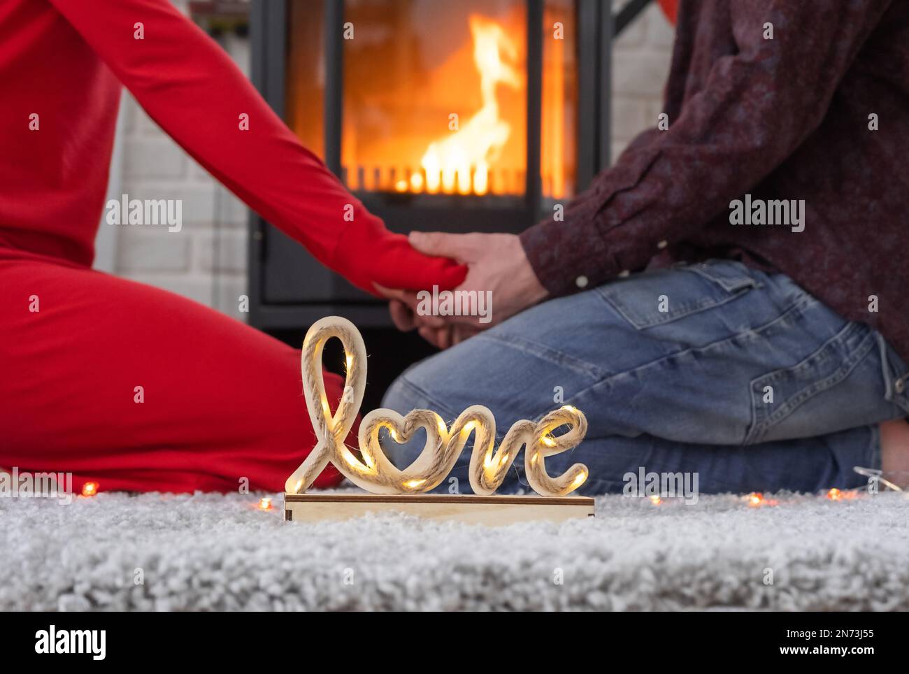 Man and woman in love date at home are sitting near the fireplace stove with a burning fire on a cozy rug. Valentine's Day, happy couple, love story, Stock Photo