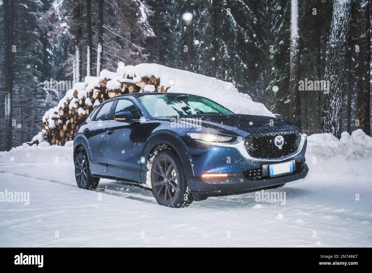 Italy, Veneto, Belluno, a Mazda Motor Corp. CX-30 crossover sport utility vehicle (SUV) on a mountain road in winter during a snowfall, Dolomites Stock Photo