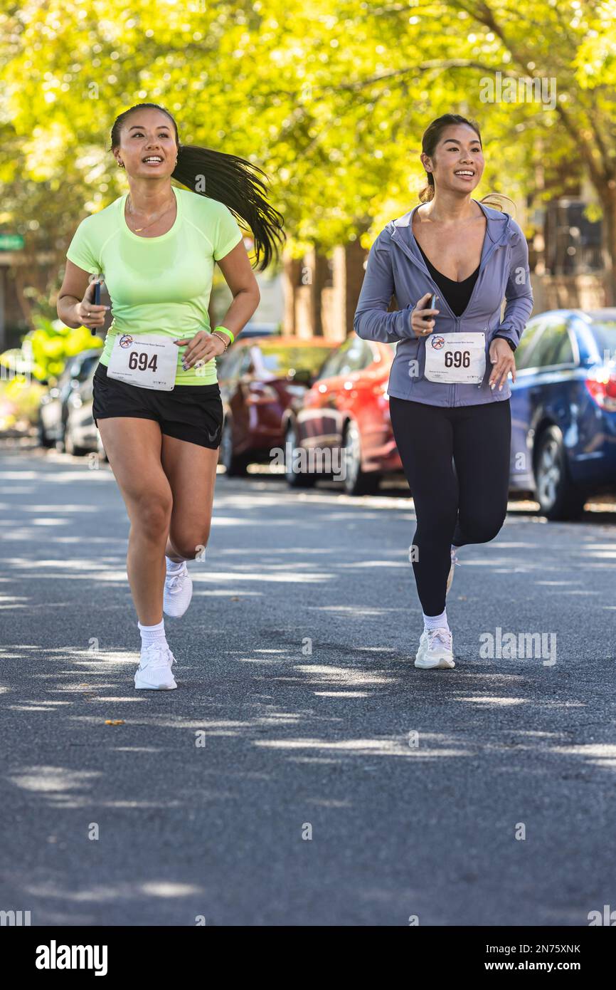 Suwanee, GA / USA - October 15, 2022:  Two young Asian American women run down residential street as they near the finish line of a 5K race. Stock Photo