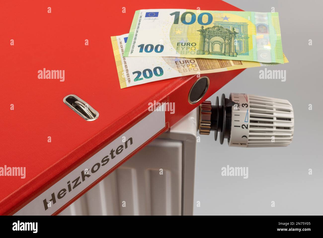 Red file folder with label heating costs, euro bills lie on radiator, symbol image, 300 euro energy flat rate, energy costs, rising heating costs, white background, Stock Photo
