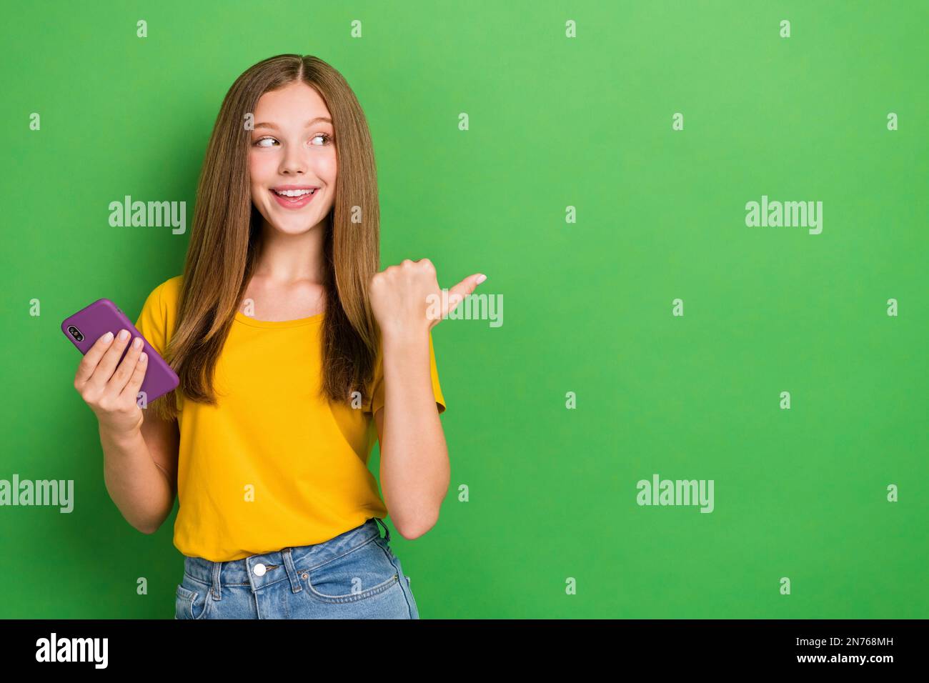 Photo of youngster teenager brown hair lady wear stylish t-shirt hold smartphone finger point look empty space isolated on green color background Stock Photo