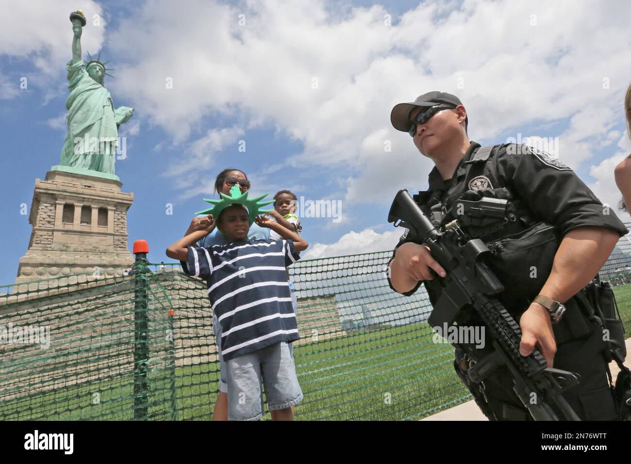 A member of the United States Park police swat team members stand guard at  the Statue of Liberty as visitors pose for photos, Thursday, July 4, 2013  at in New York. The