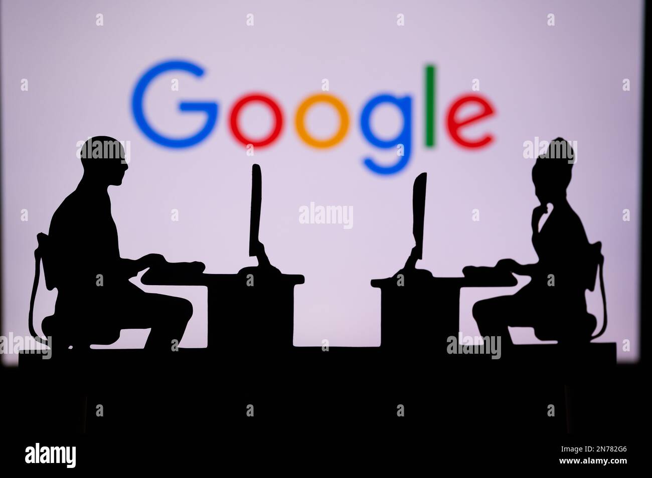 UK, LONDON. JANUARY 30, 2023: Google. Pushing Boundaries with Cutting-Edge Software: Two Developers Silhouetted with Company Logo in Background. Stock Photo