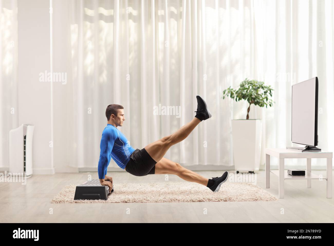 Bodybuilder exercising planks with a stepper in front of tv at home Stock Photo
