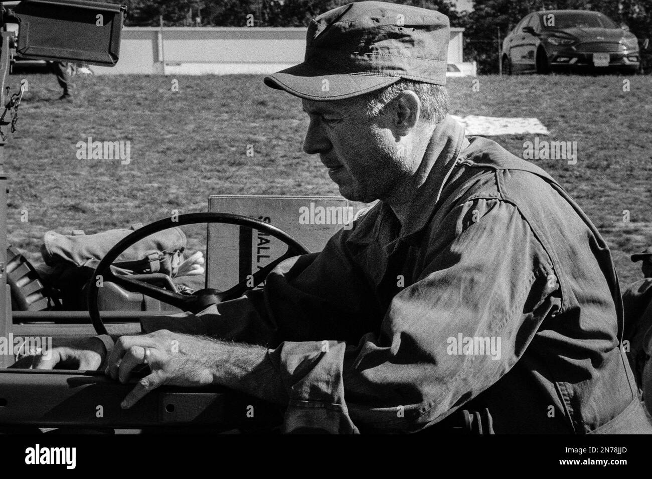 A WWII soldier resting his upper body against a Jeep during a reenactment at the American Heritage Museum. The image was captured on analog black and Stock Photo