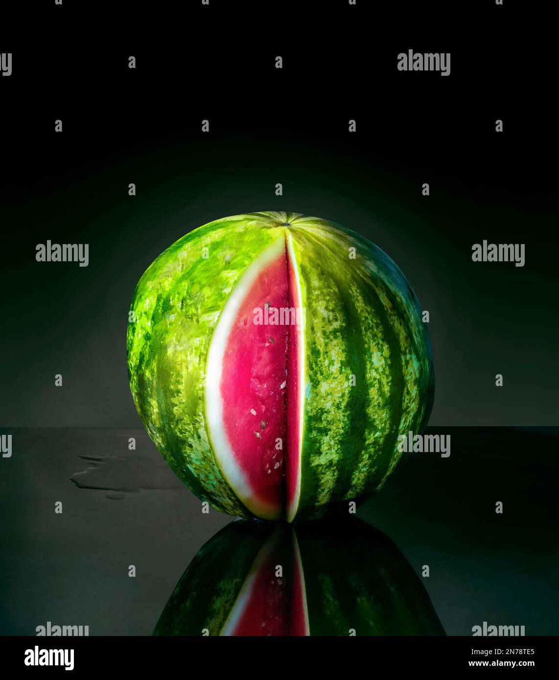 Watermelon with a slice removed, with reflection, isolated on dark background Stock Photo