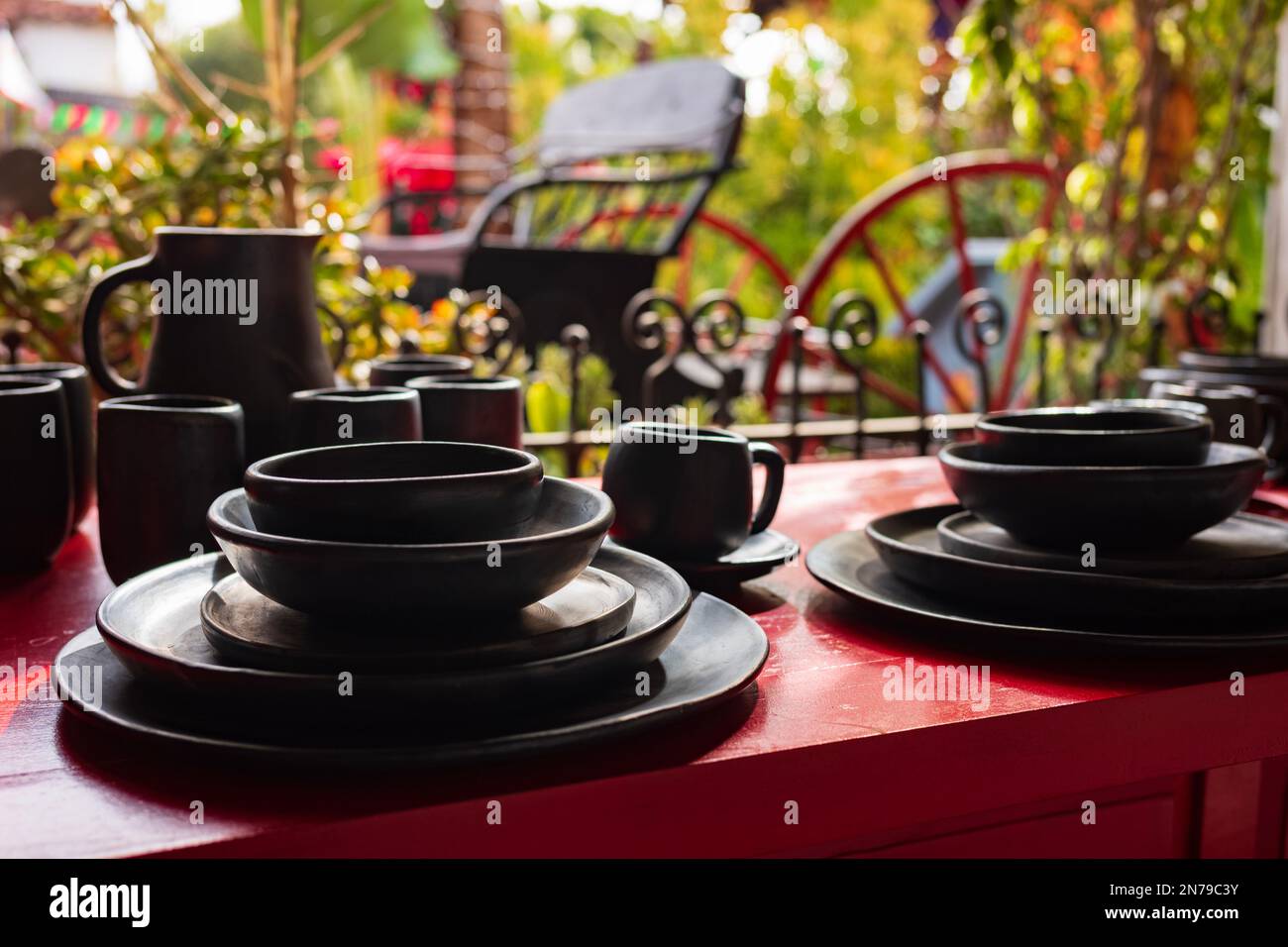 A dining set painted black rests on a red table outside with green vegiation serving as a backdrop. Stock Photo