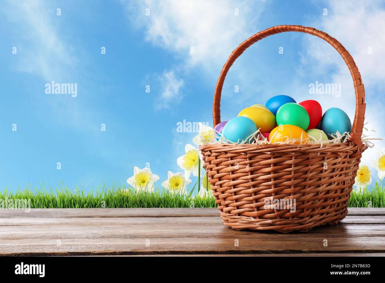 Colorful Easter eggs in wicker basket on wooden table outdoors, space ...