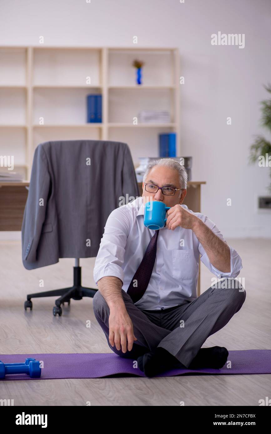 Old employee doing sport exercises during break Stock Photo