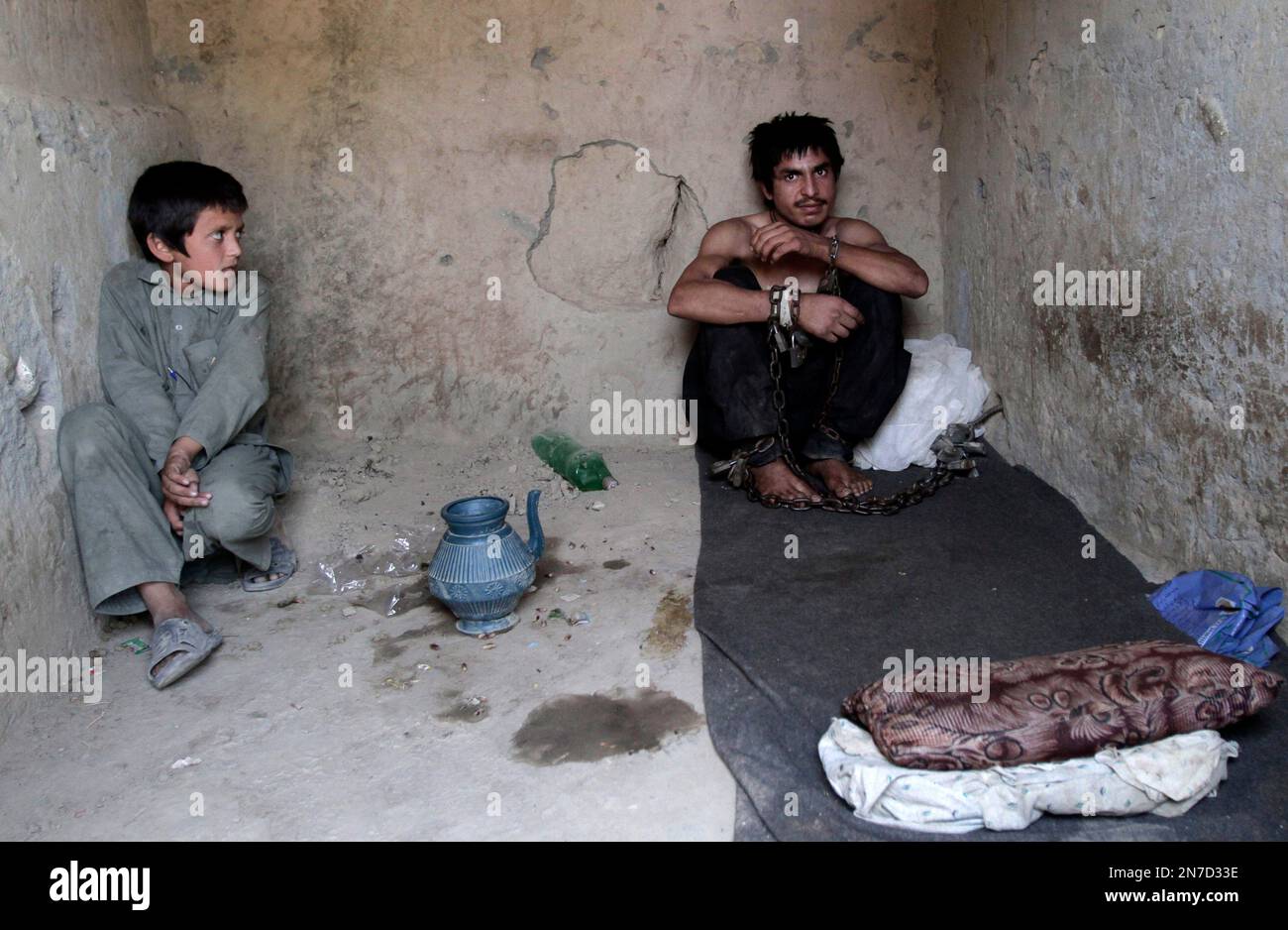 A village boy watches Nabiullah Safi, 23, a drug addict, who is chained