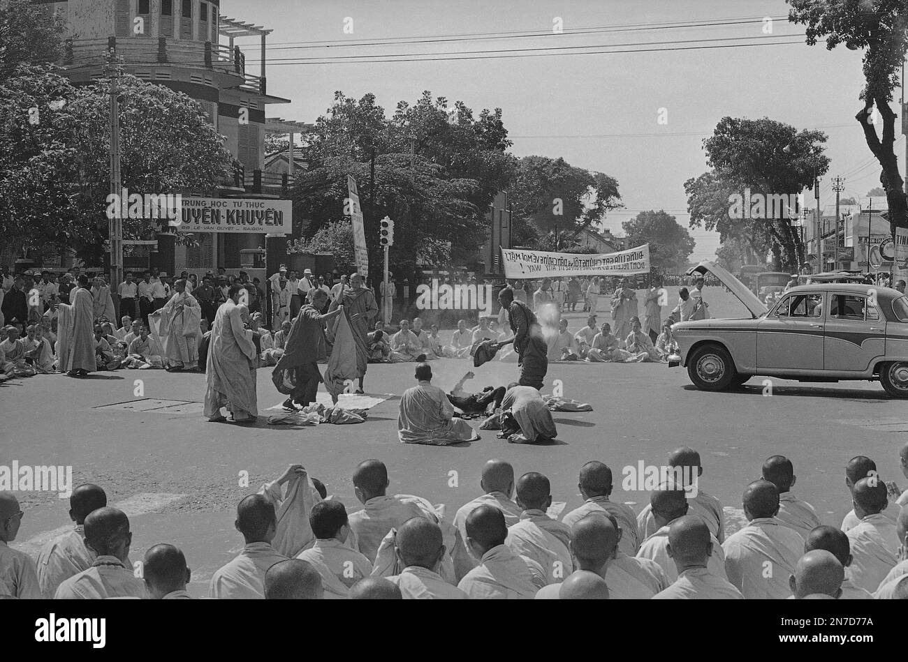 EDS NOTE: GRAPHIC CONTENT - This crowd in a main intersection of Saigon, Vietnam, watched the dramatic burning to death of an elderly Buddhist monk, Rev. Thich Quang Duc, June 11, 1963. As this picture was taken the flames from the monk's gasoline-soaked robes had died down and the charred body of the suicide lay in the street. Other monks approach to wrap his body in a Vietnamese flag. The monk's act was a public protest of alleged persecution of Buddhists by the Vietnamese government. (AP Photo/Malcolm Browne) Stock Photo