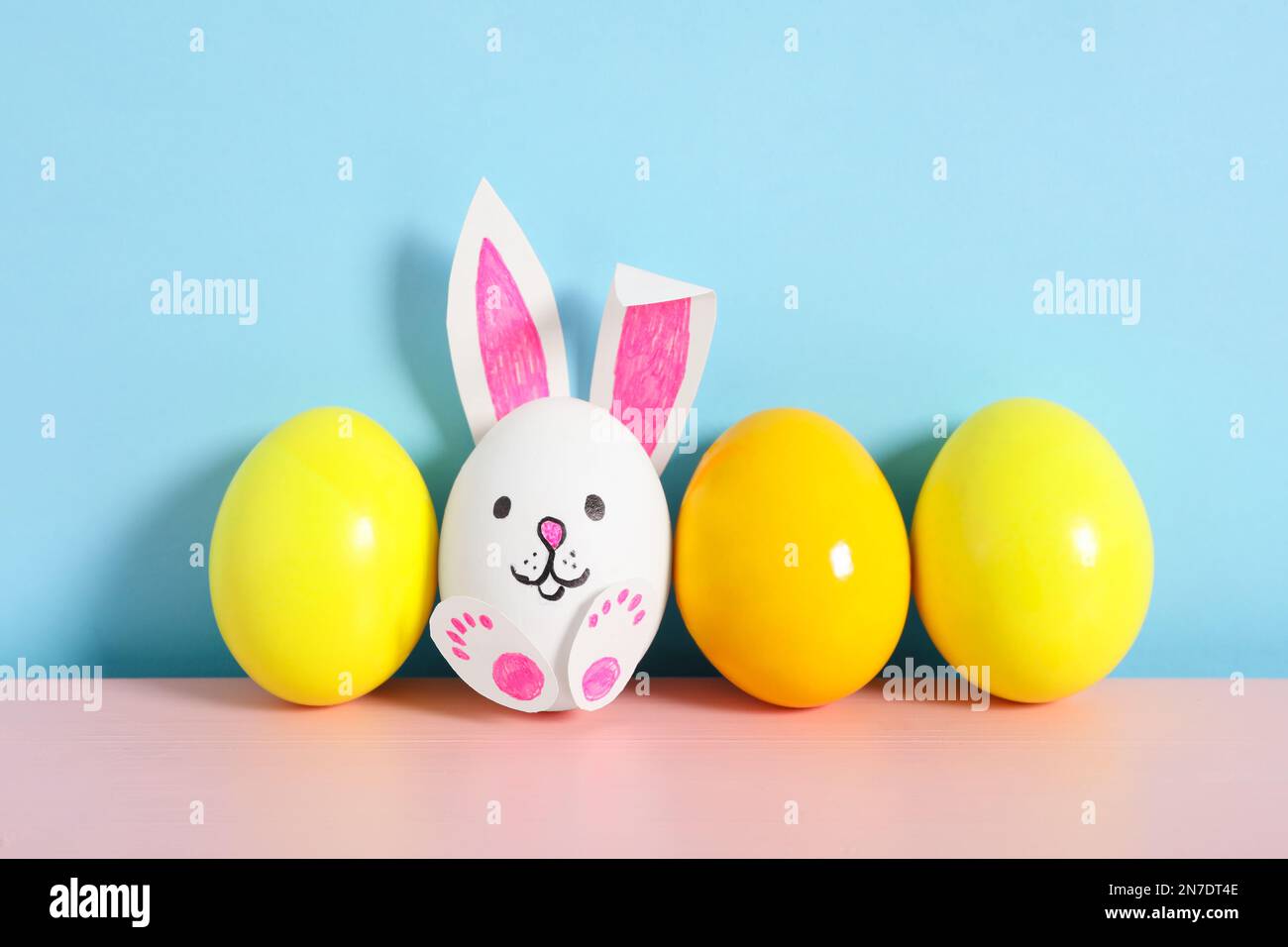 Bright eggs and white one as cute bunny on pink wooden table against ...