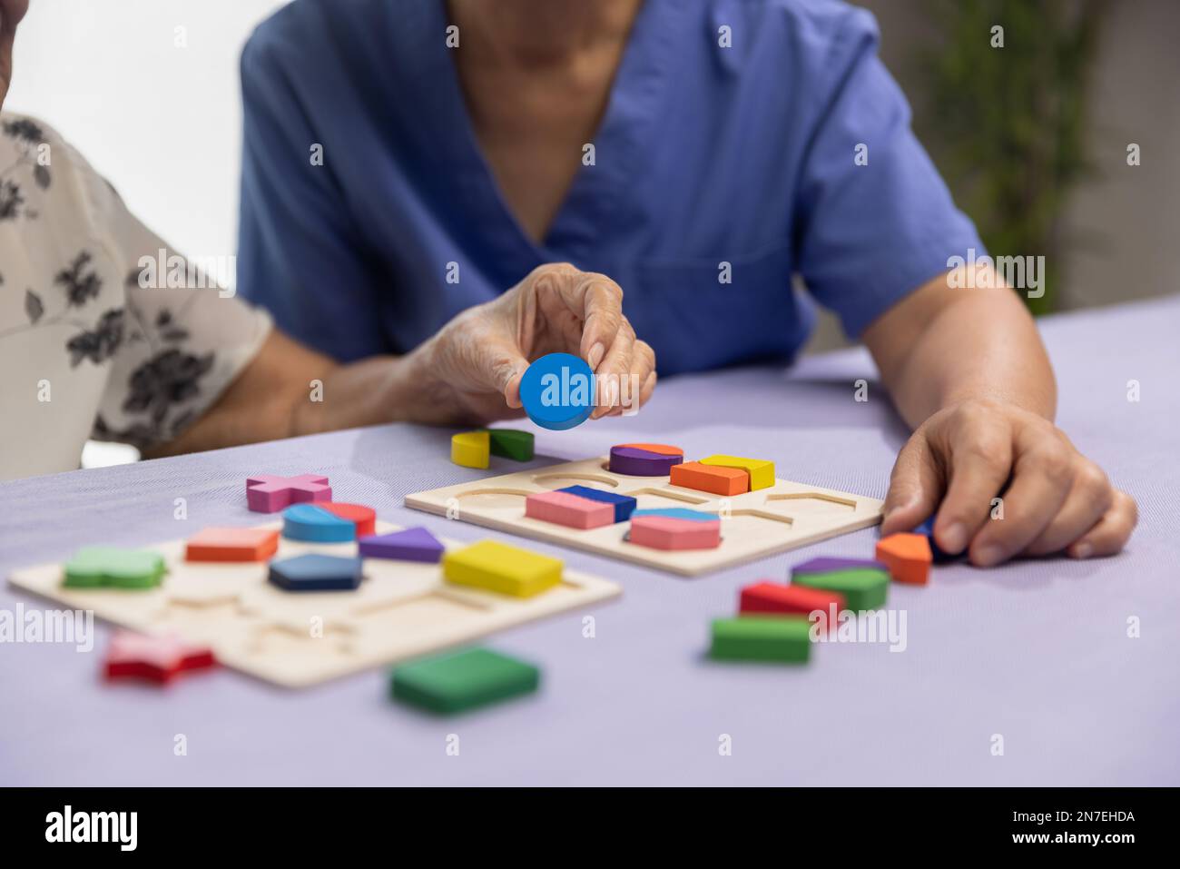 Caregiver and senior woman playing wooden shape puzzles game for