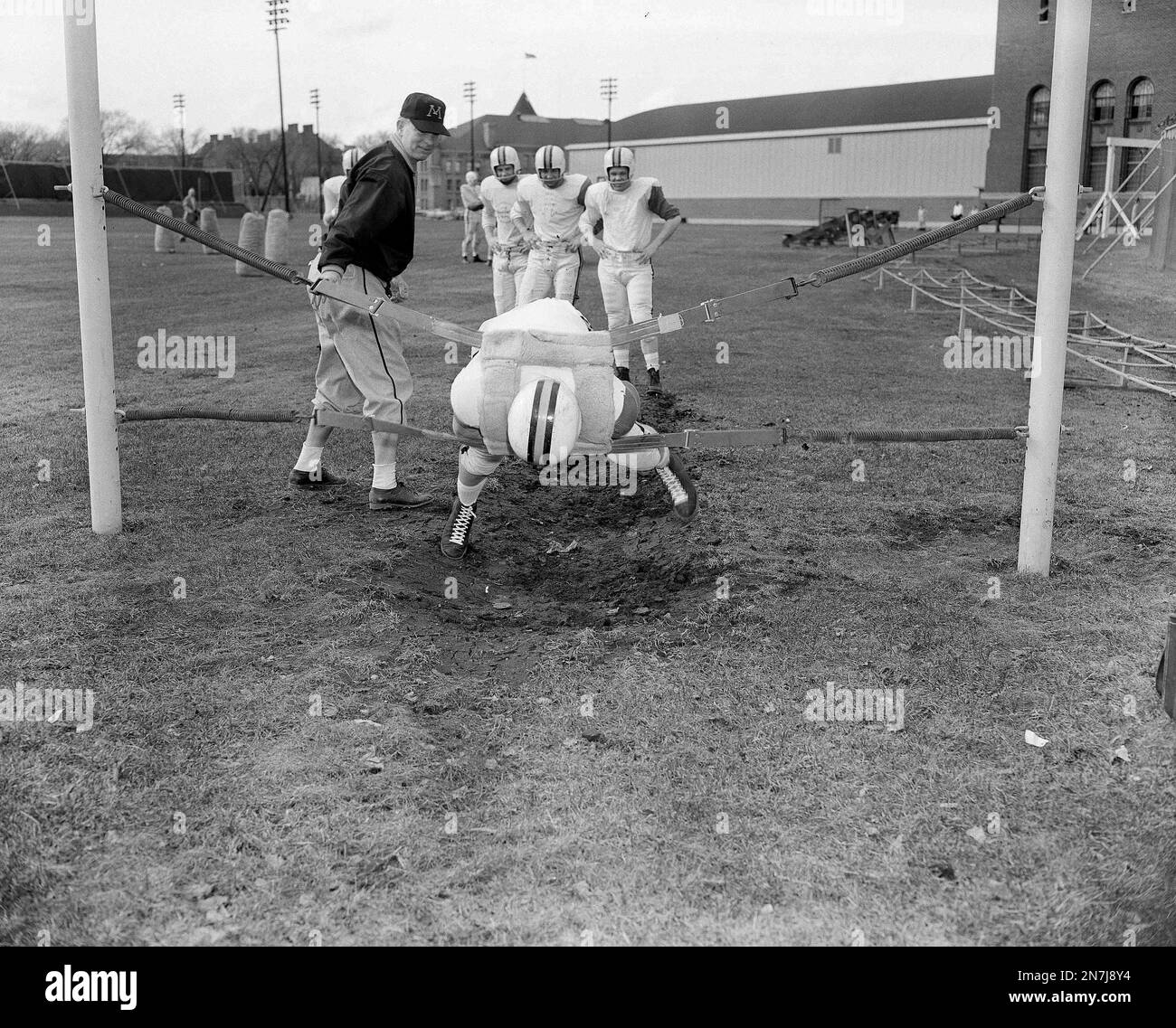 Minnesota's backfield coach Billy Murphy, left, watches as Dick Borstad hits the harness during spring training on the Gophers' field in Minneapolis, April 24, 1957. (AP Photo/George Hill) Stock Photo